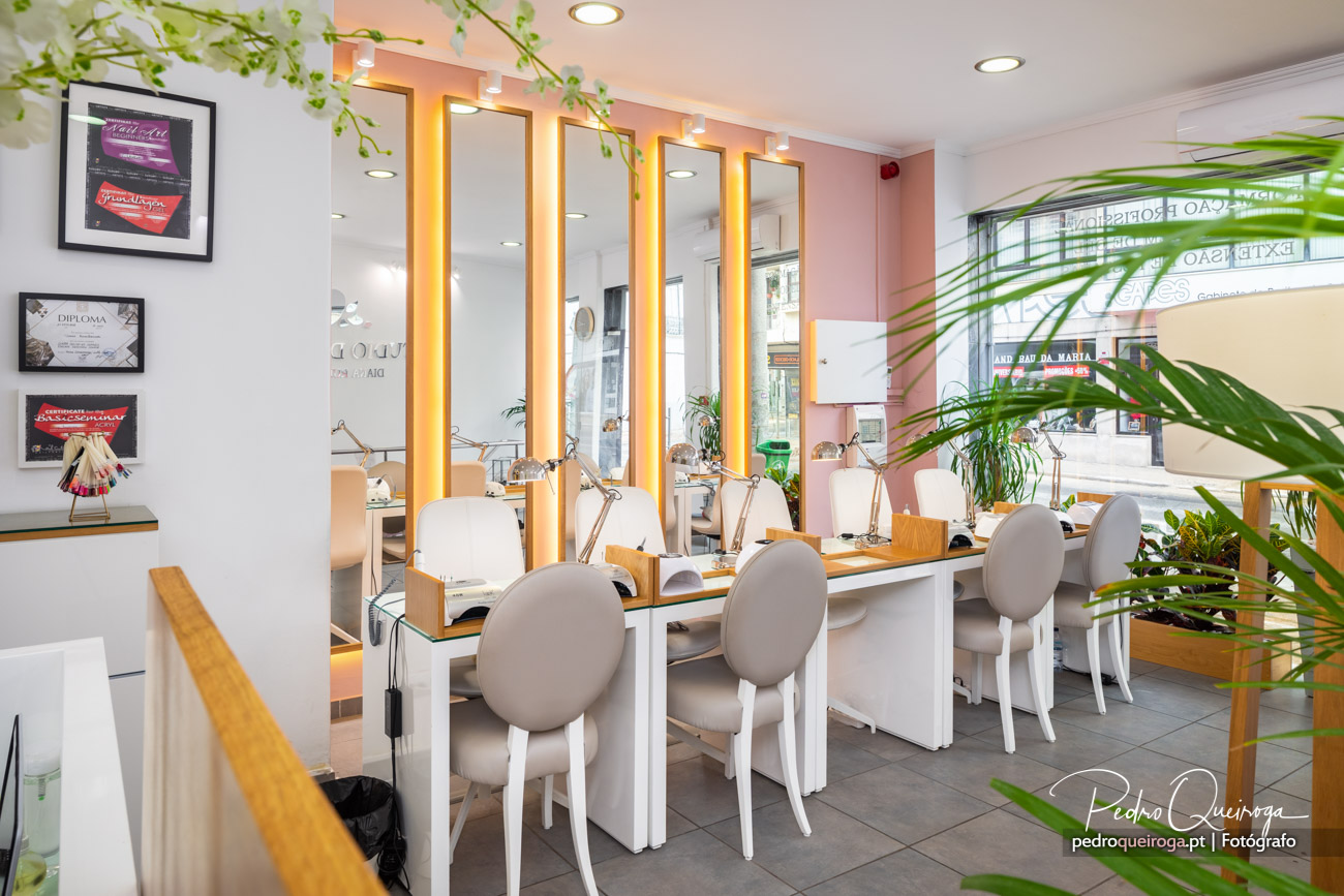 Interior moderno de salão de beleza com espelhos iluminados, cadeiras brancas, plantas decorativas e tons rosa suave