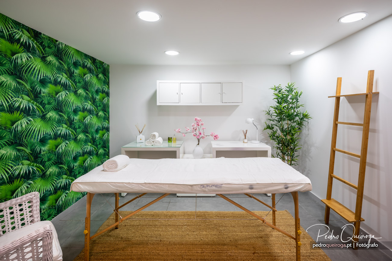 Sala de massagens moderna com maca branca, papel de parede tropical verde e decoração minimalista em tons naturais