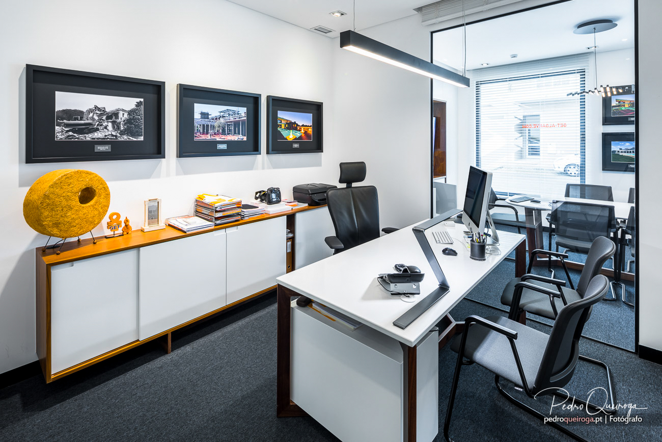 Escritório moderno com secretária branca, cadeiras cinzentas, quadros emoldurados na parede e escultura amarela decorativa