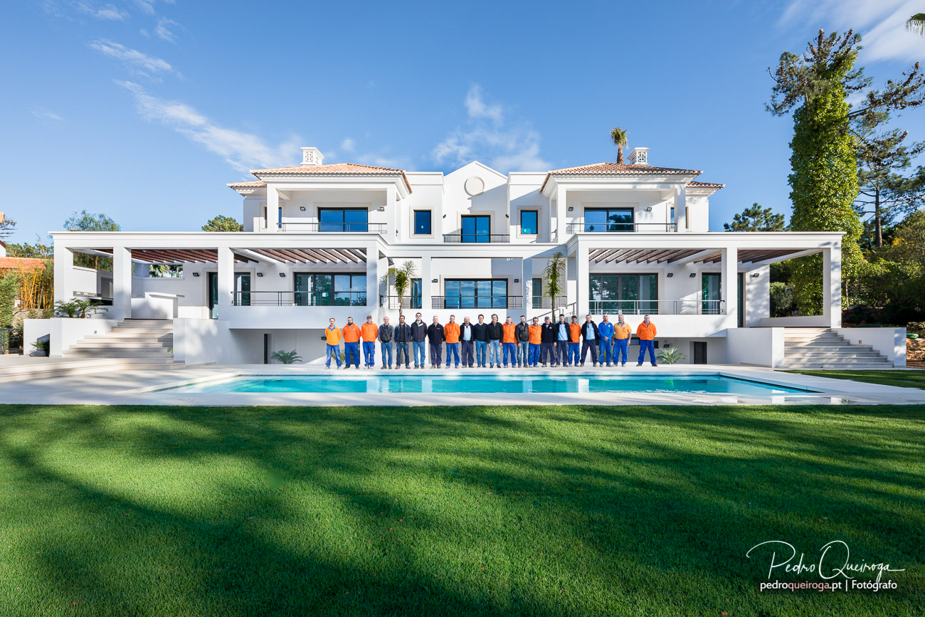 Moradia moderna branca com piscina e equipa de construção posicionada em frente à fachada principal