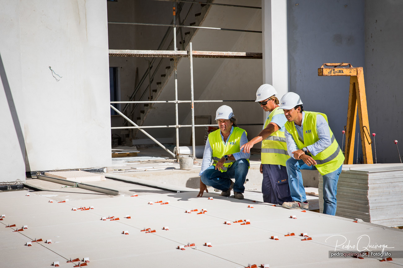 Três profissionais em obra examinam o pavimento numa sessão de reportagens fotográficas industriais em Portugal