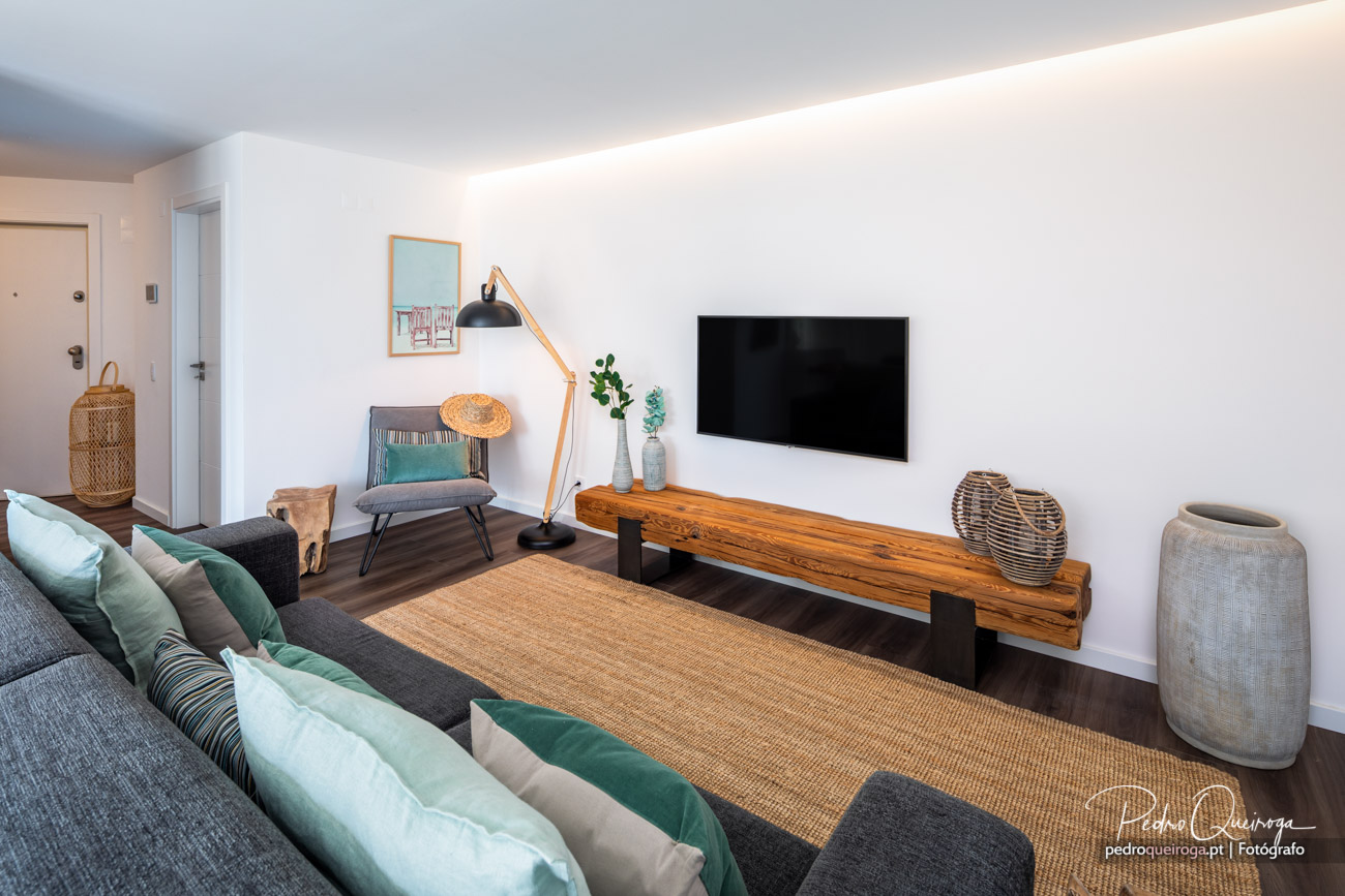 Sala de estar moderna com sofá verde, móvel de madeira sob televisão e decoração em tons naturais e minimalistas