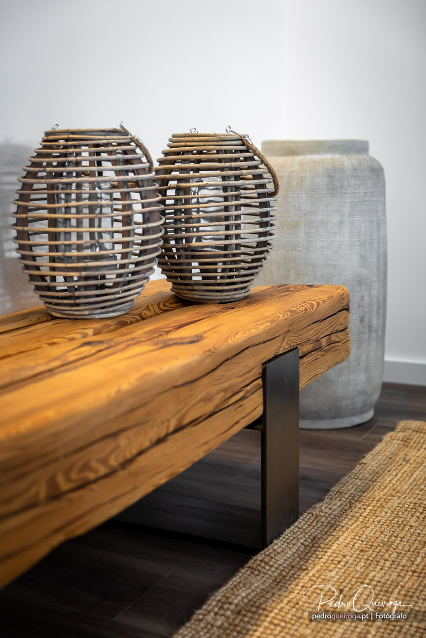 Duas lanternas em vime repousam sobre mesa de madeira rústica, captadas pelo fotógrafo em ambiente minimalista.