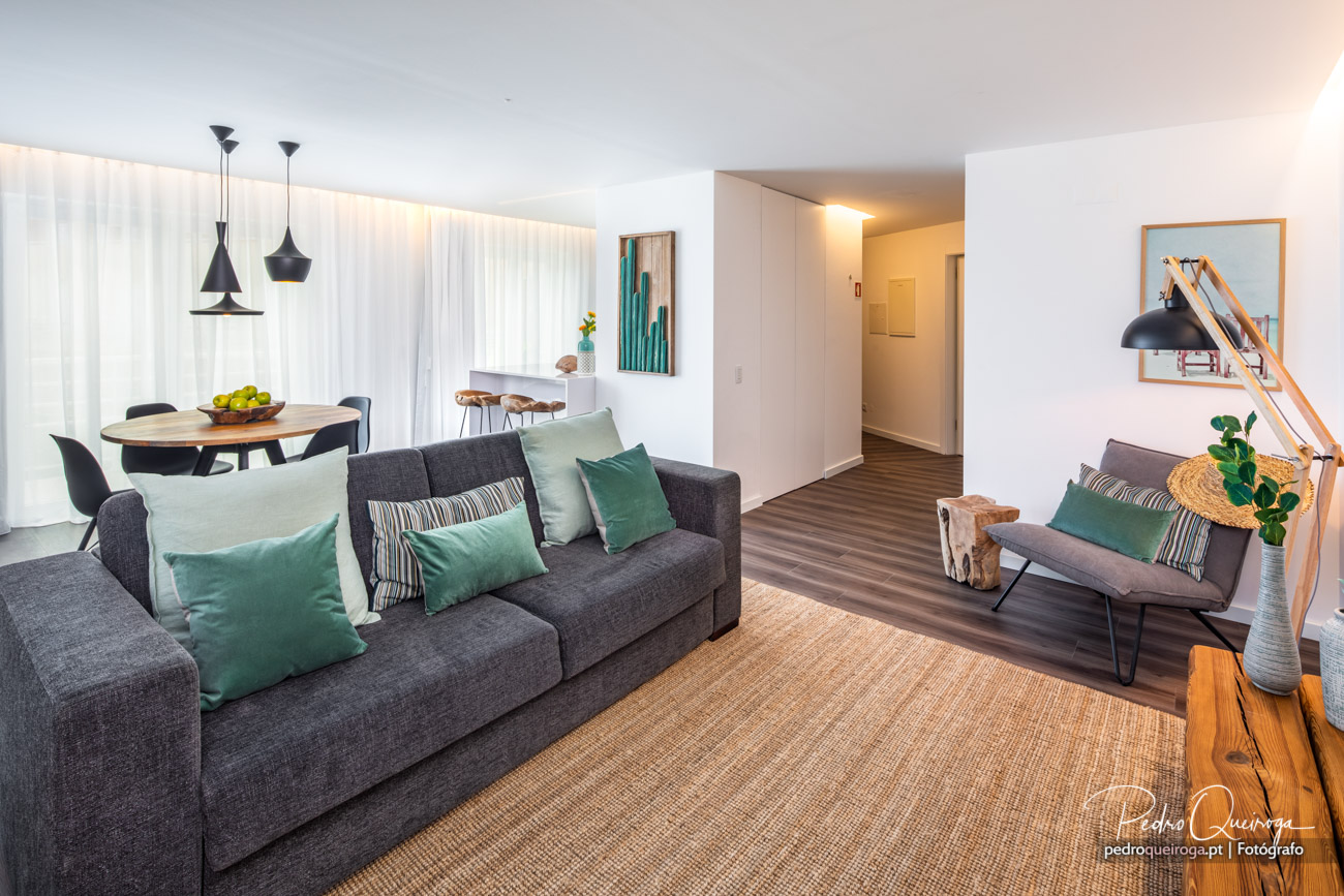 Sala de estar moderna com sofá cinzento, almofadas verdes, mesa de jantar redonda e luminária de madeira junto à janela.