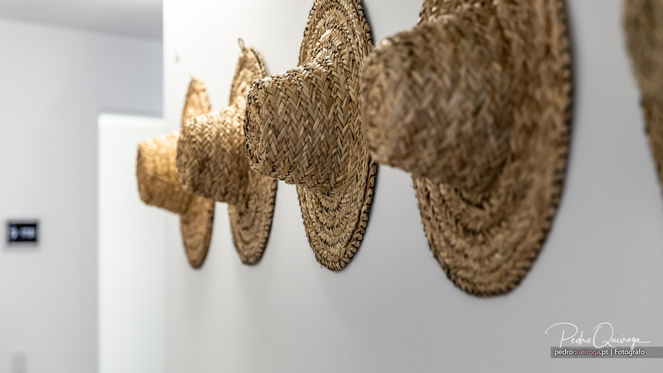 Chapéus de palha artesanais suspensos numa parede branca, revelando texturas e padrões entrelaçados naturais