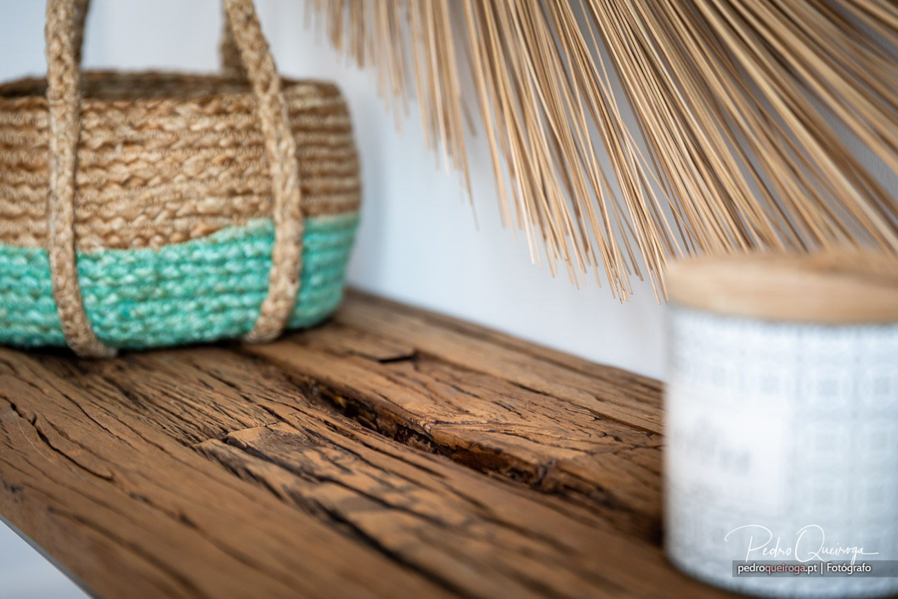 Prateleira rústica em madeira com saco de praia turquesa e natural, junto a chapéu de sol de palha.