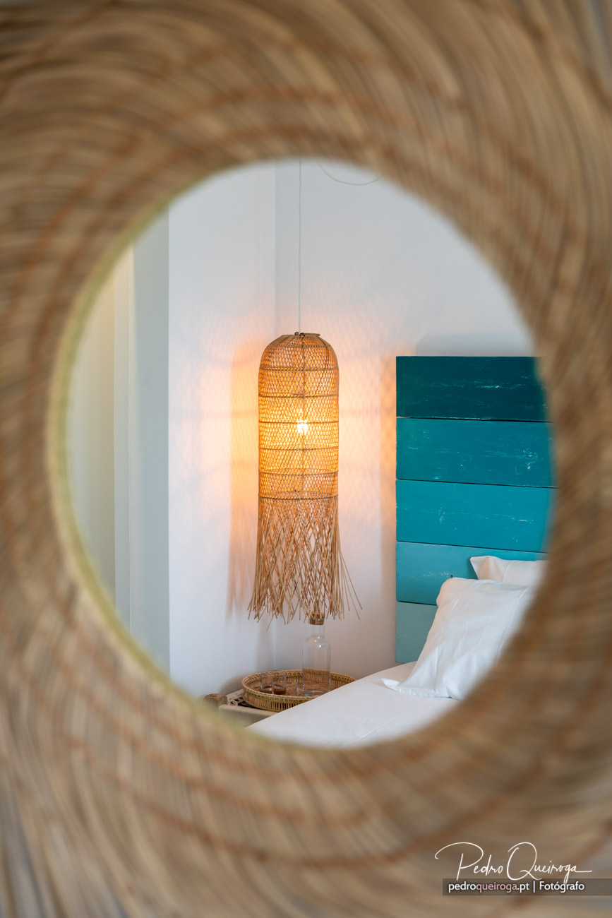 Quarto de hotel com candeeiro de vime suspenso, parede turquesa e roupa de cama branca, ideal para hotéis boutique