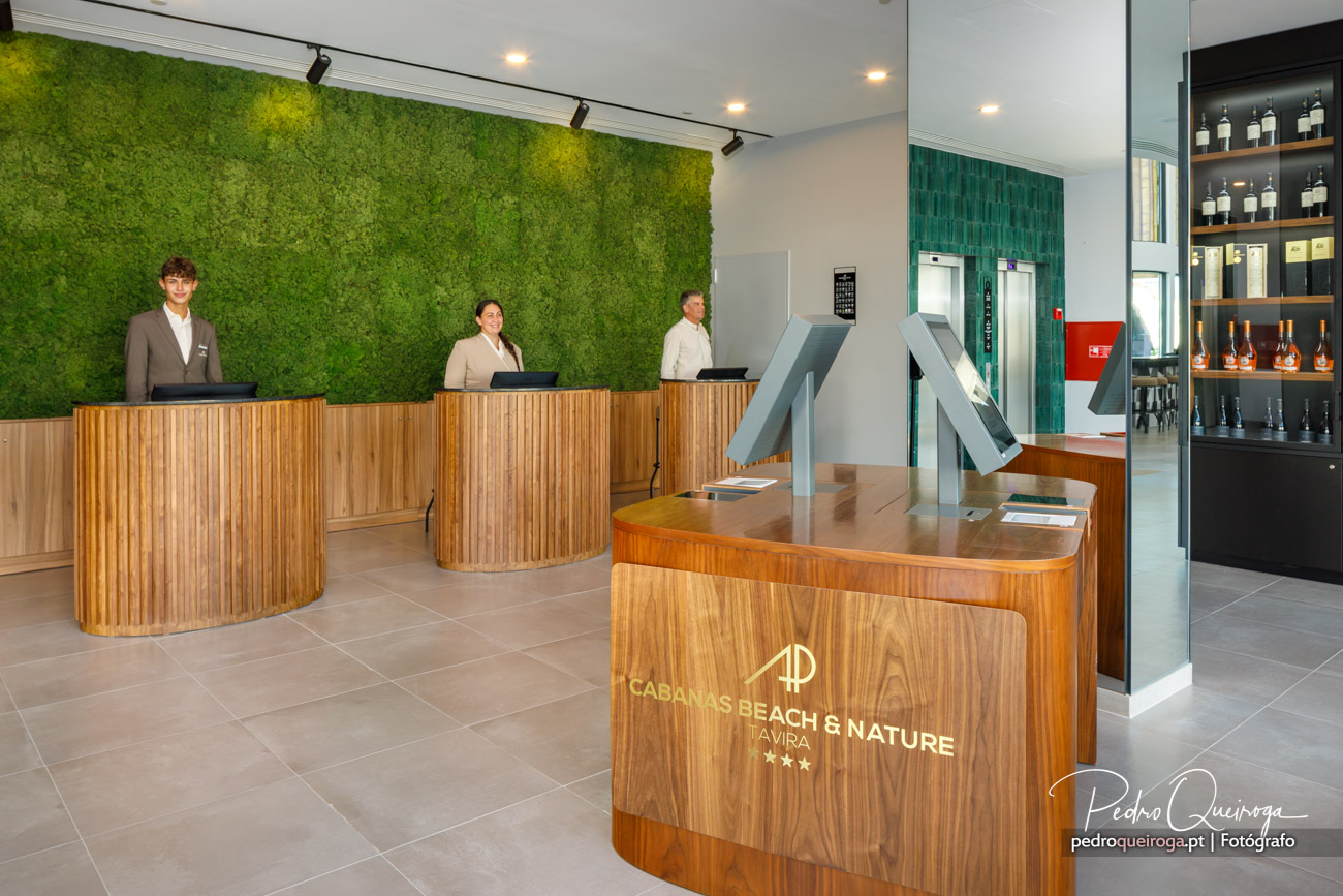 Receção moderna com balcão em madeira, parede verde vertical e equipa de três colaboradores em ambiente elegante