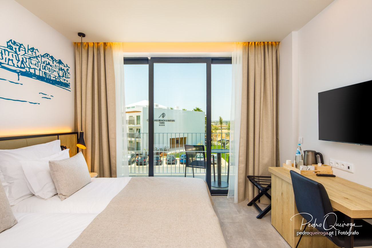 Quarto moderno com varanda envidraçada, cama de casal, secretária em madeira e iluminação ambiente quente e acolhedora.