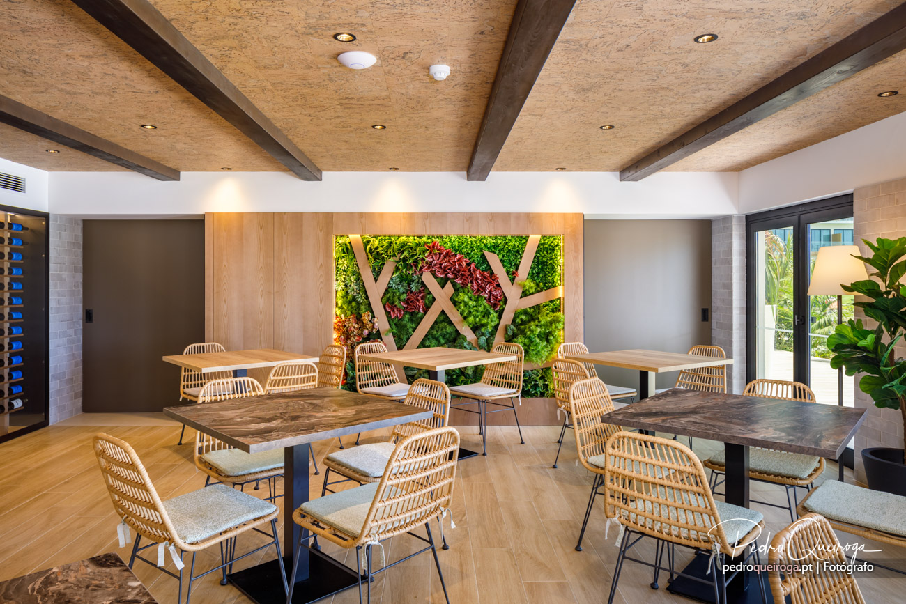 Sala de refeições moderna com mesas de madeira, cadeiras em rattan e parede verde vertical com padrão geométrico decorativo