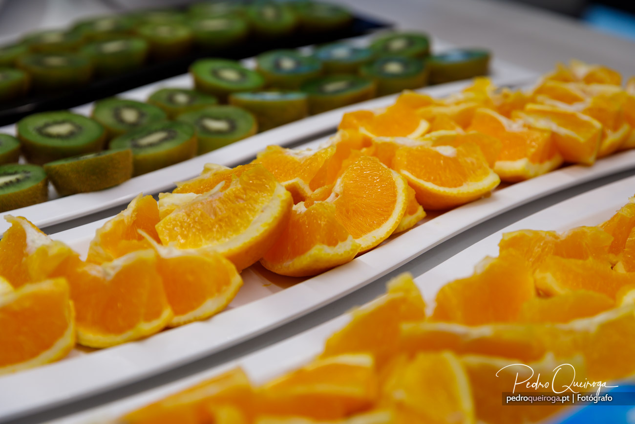 Rodelas de laranja e kiwi fatiados dispostos em travessas brancas alongadas sobre uma mesa