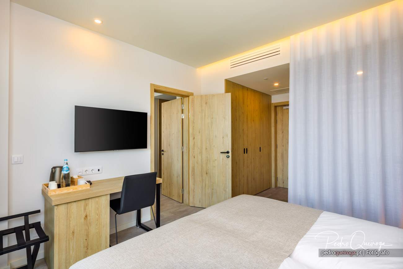 Quarto moderno com madeira clara, secretária, TV e casa de banho integrada - fotografia de interiores