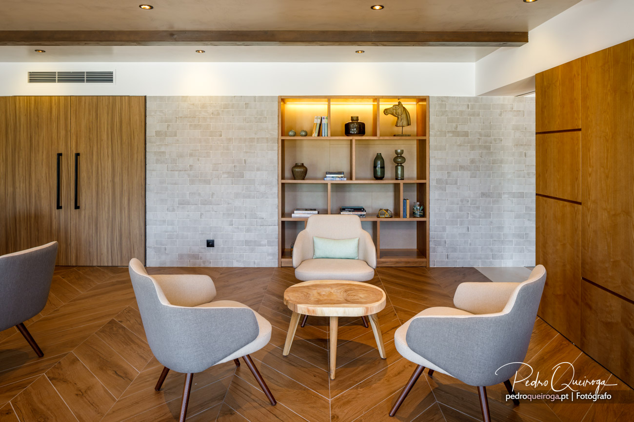 Sala de estar moderna com poltronas cinzentas, estante iluminada e paredes em tijolinho no interior do imóvel