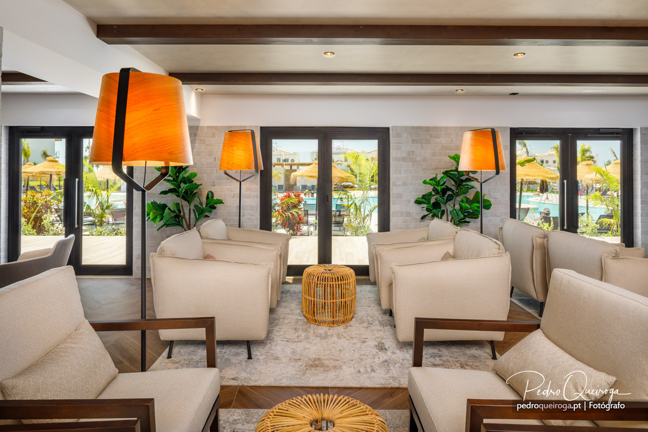 Sala de estar luminosa com sofás bege, candeeiros laranja e vista para piscina através de portas envidraçadas