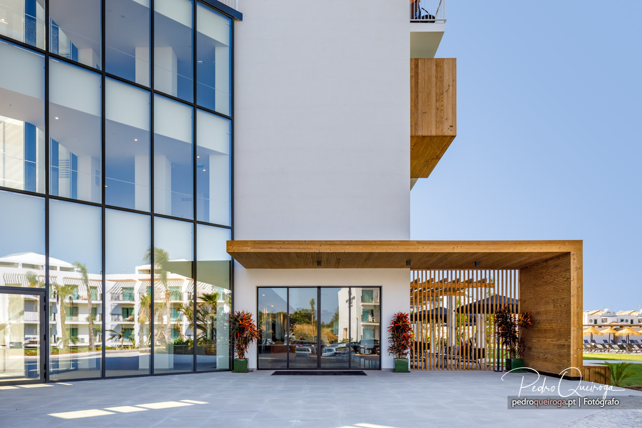 Fachada moderna com grandes janelas e revestimento em madeira sob céu azul num dia ensolarado.
