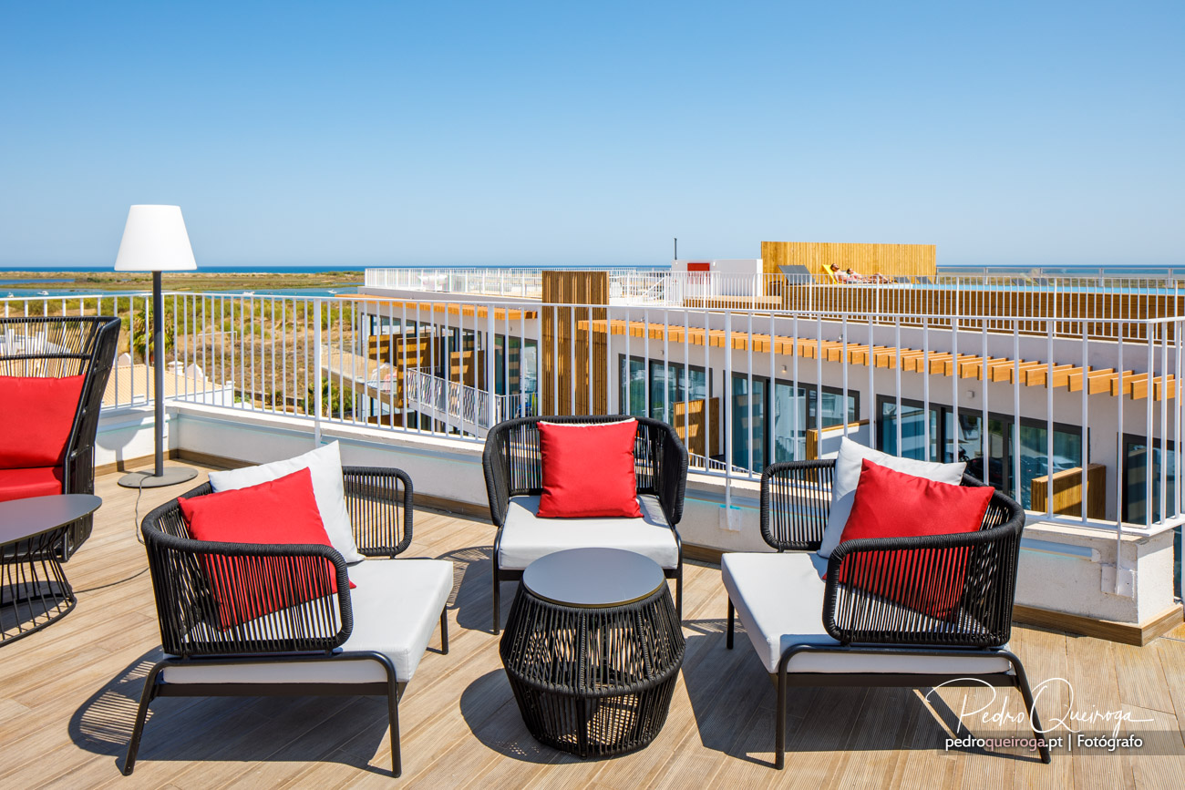 Terraço moderno com lounge, almofadas vermelhas e vista fotográfica sobre resort e mar ao fundo