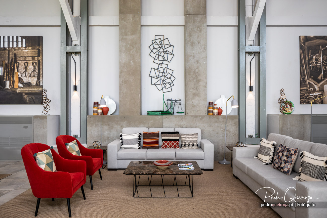 Sala de estar moderna com sofás cinzentos, poltronas vermelhas, pilares de betão e arte contemporânea nas paredes