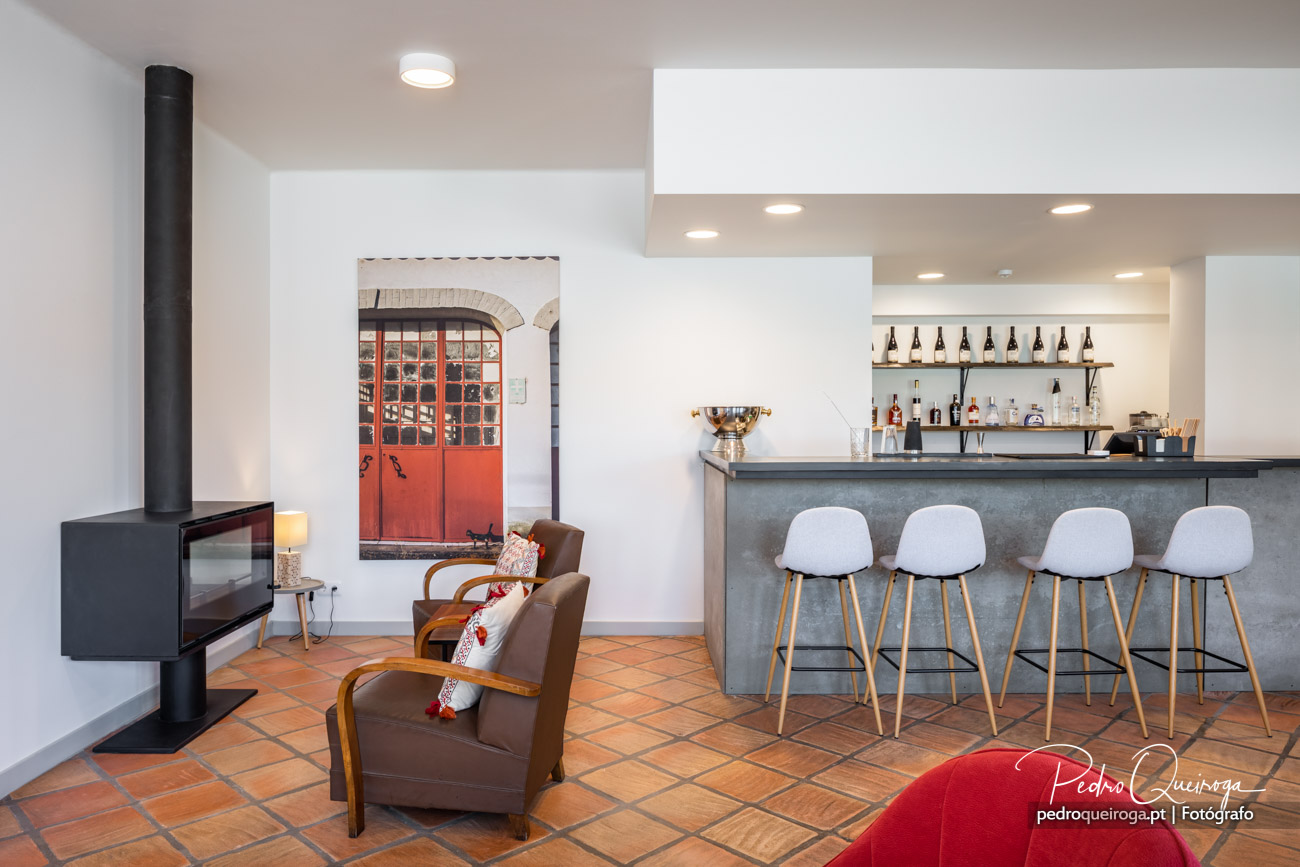 Sala ampla com lareira moderna, porta vermelha antiga emoldurada, bar com bancos brancos e chão em terracota
