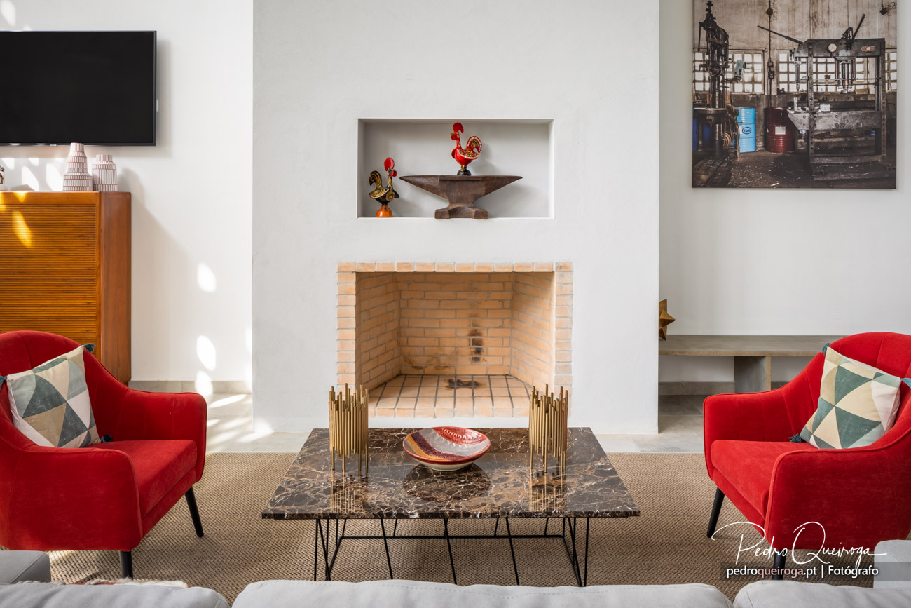 Sala de estar com lareira em tijolo, poltronas vermelhas e mesa de centro em mármore escuro com detalhes dourados.