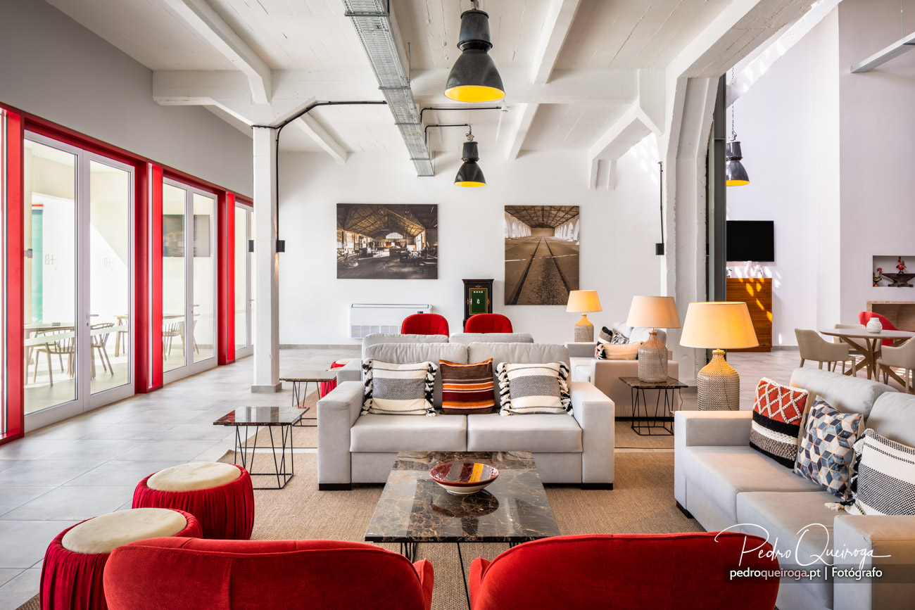 Sala de estar ampla com sofás cinza, cadeiras vermelhas, portas vermelhas e candeeiros industriais amarelos suspensos