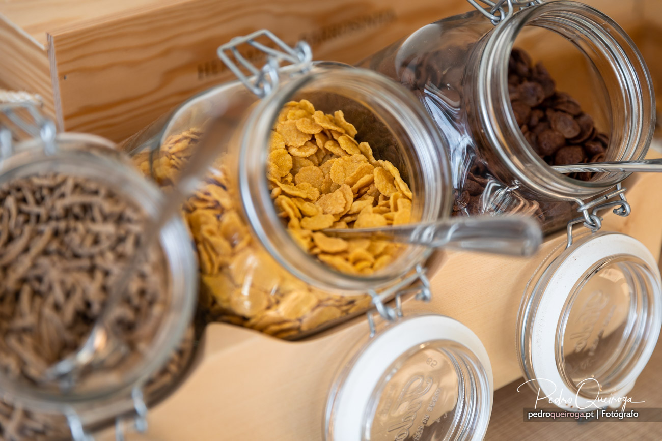 Frascos de vidro com cereais e chocolate sobre bancada de madeira, típicos de imóveis com cozinha acolhedora