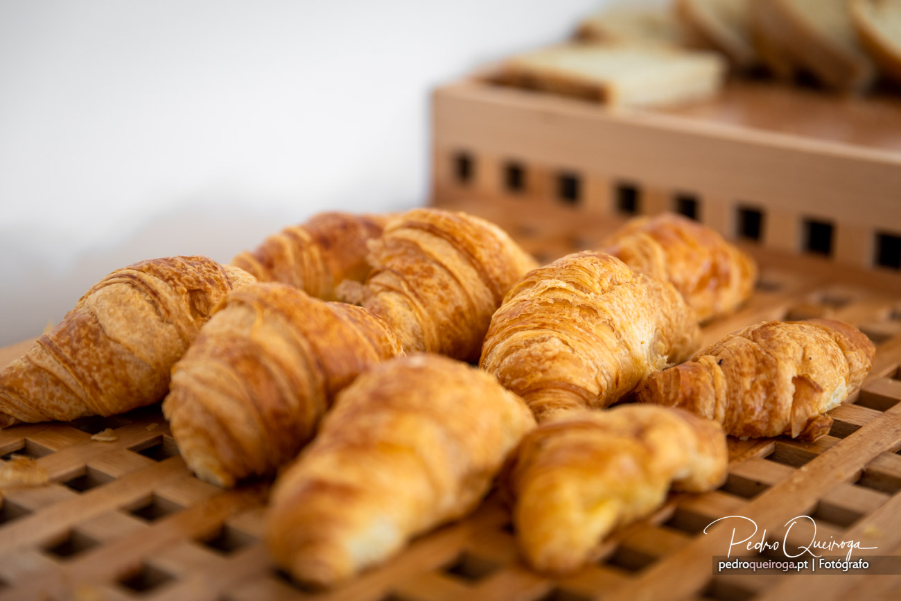 Croissants dourados e estaladiços dispostos sobre tabuleiro de madeira, prontos a saborear num ambiente acolhedor