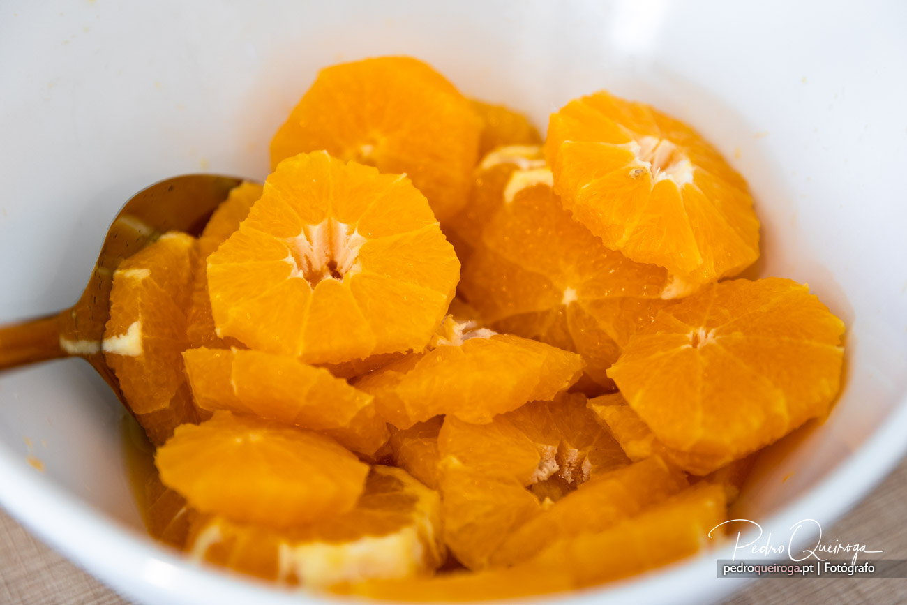Rodelas de laranja descascadas numa taça branca, com colher de madeira, em tons vibrantes de cor de laranja