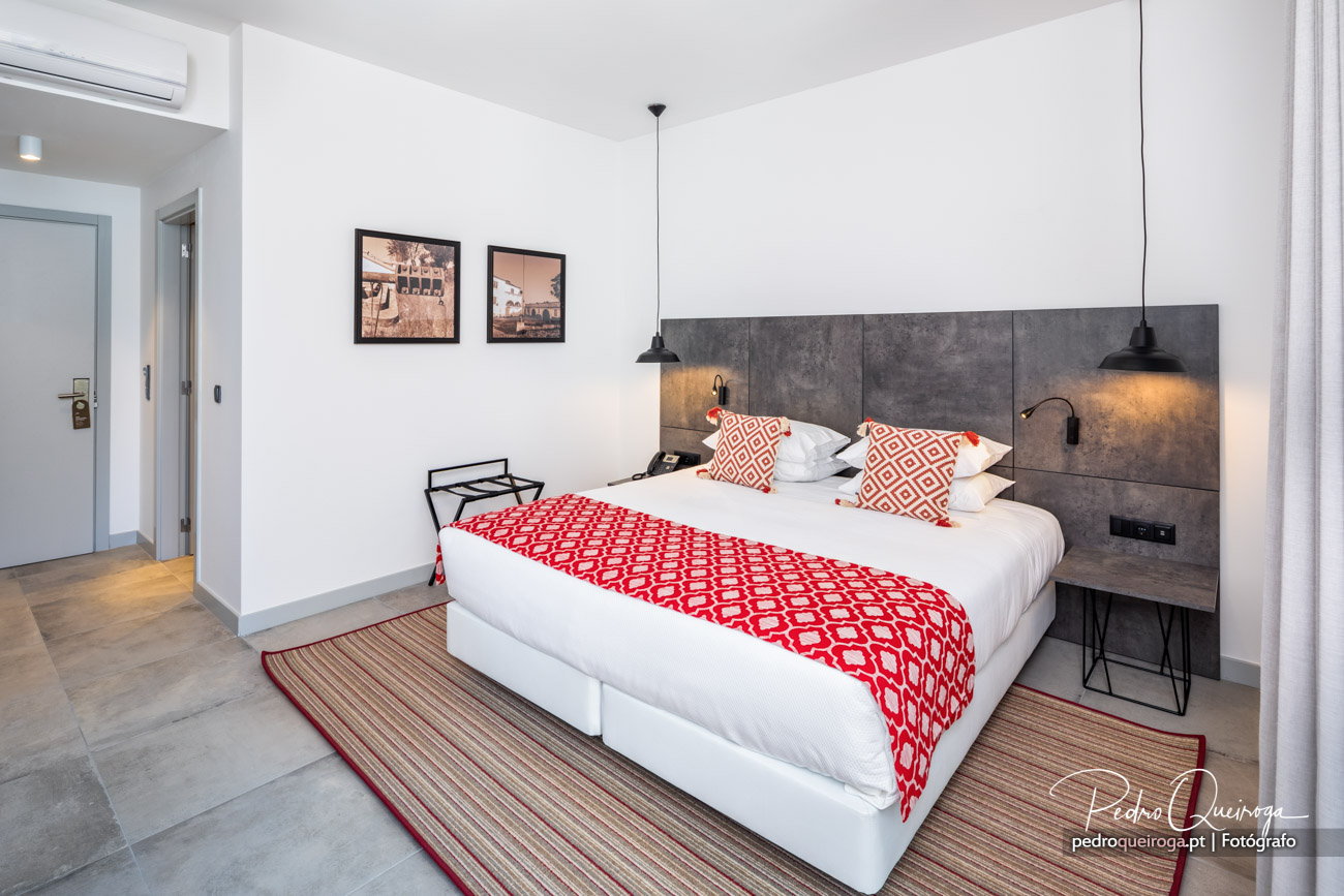 Quarto moderno com cama branca, colcha vermelha geométrica, cabeceira cinza e candeeiros pendentes pretos