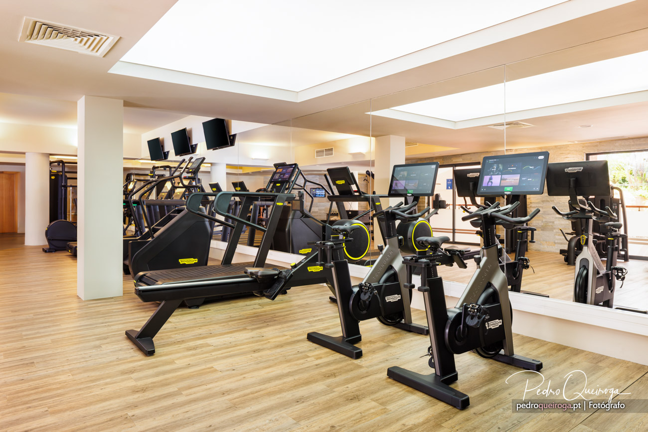 Ginásio moderno com bicicletas estáticas, passadeiras e equipamento cardio sob claraboia ampla e acabamentos em madeira clara