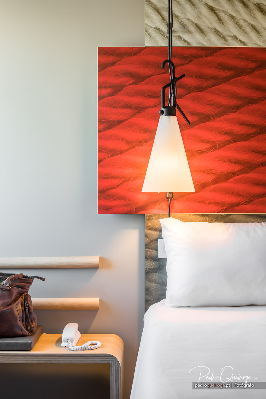 Quarto moderno com parede vermelha texturizada, candeeiro suspenso branco e roupa de cama imaculada.