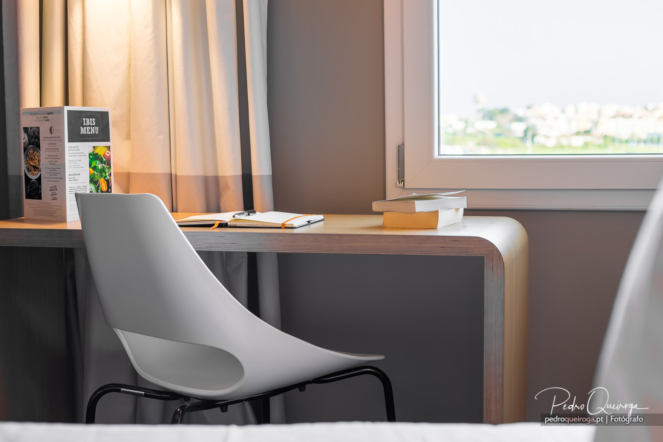 Secretária moderna junto à janela em quarto de hotel, ideal para fotografar imóveis com luz natural suave