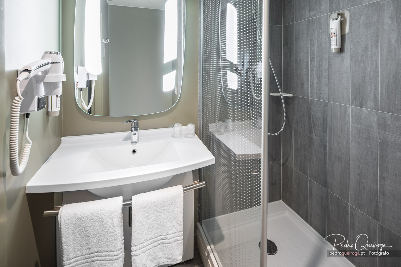 Casa de banho moderna com lavatório branco, espelho arredondado, duche com mosaico texturizado e toalhas imaculadas.