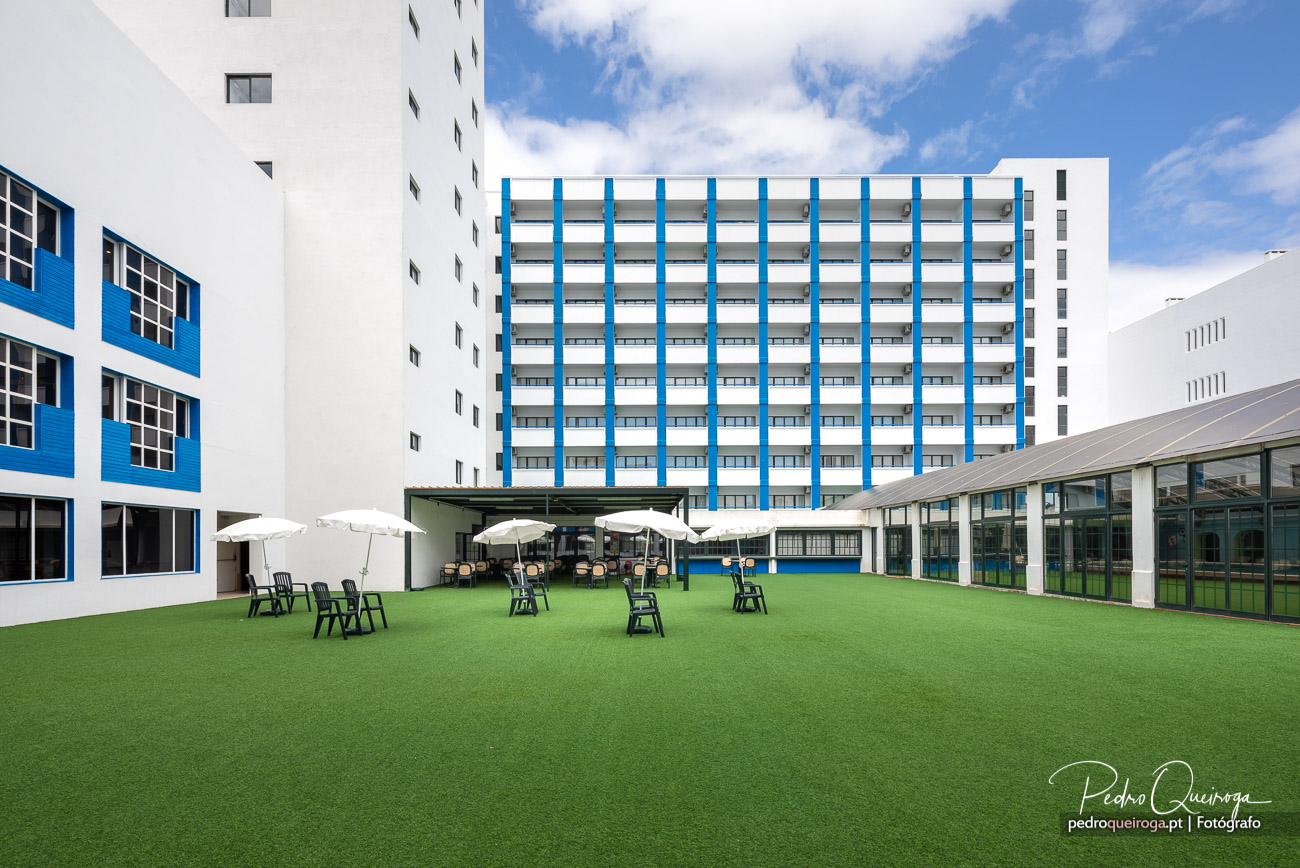 Espaço exterior moderno com relvado sintético e esplanada entre edifícios brancos e azuis