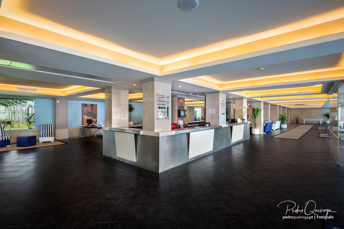 Receção moderna de hotel com iluminação LED dourada e balcão central, ideal para fotografia imobiliária profissional