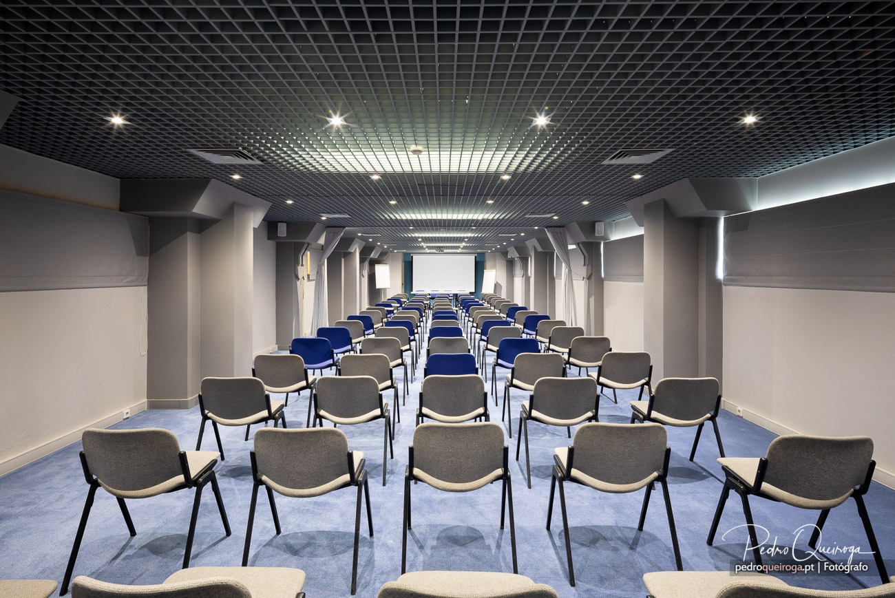 Auditório moderno com cadeiras cinzentas e azuis, ideal para reportagens fotográficas de arquitetura e espaços corporativos.