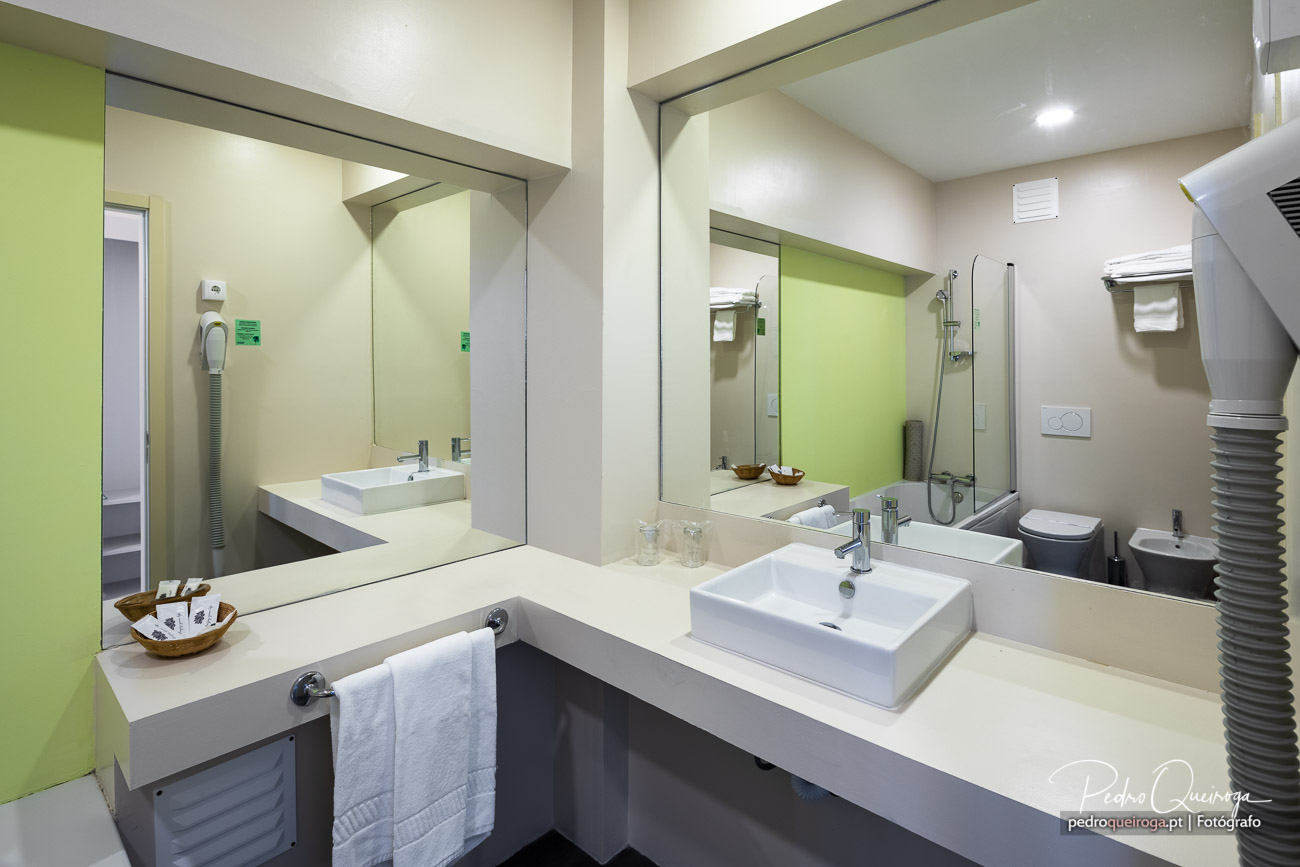 Casa de banho moderna com duplo lavatório, espelhos grandes, detalhes verdes e acabamentos minimalistas.