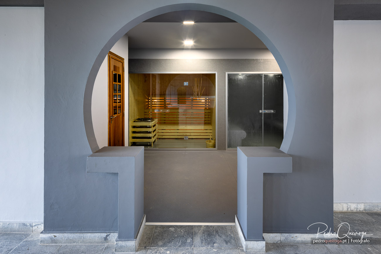 Arco em betão enquadra sauna em madeira e duche, criando uma decoração moderna e relaxante para spa privado