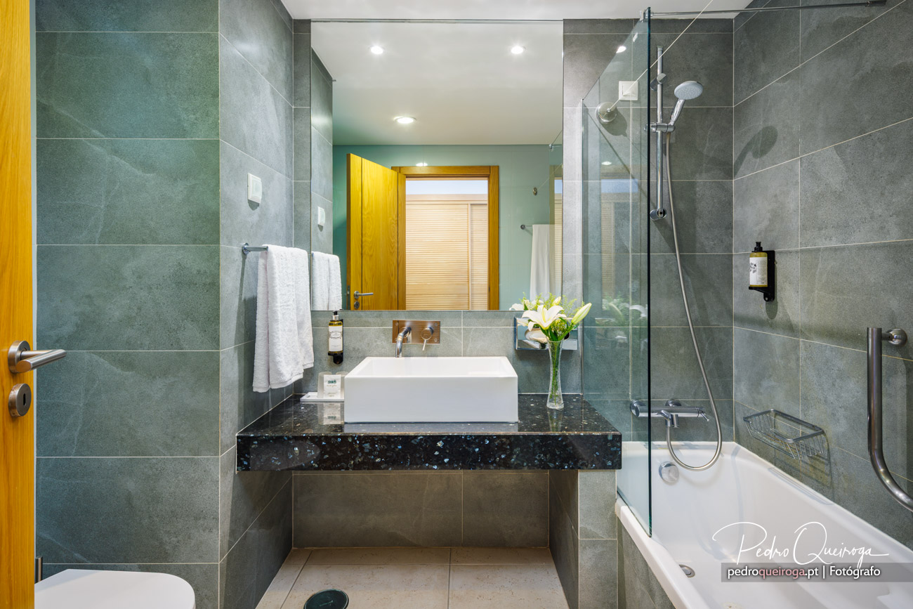 Casa de banho moderna com azulejos cinzentos, bancada preta e flores brancas em composição fotográfica elegante