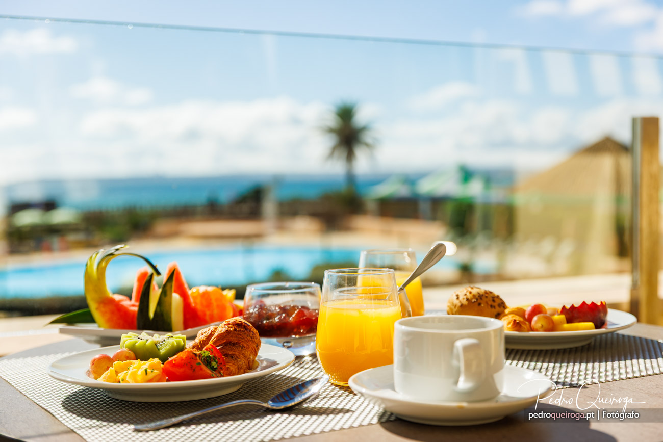 Pequeno-almoço tropical junto à piscina com croissants, fruta fresca, sumo de laranja e café sob o sol.