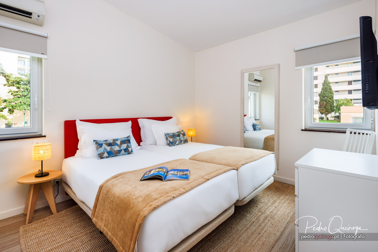 Quarto moderno com cabeceira vermelha, roupa branca, almofadas geométricas e espelho de parede amplo e luminoso