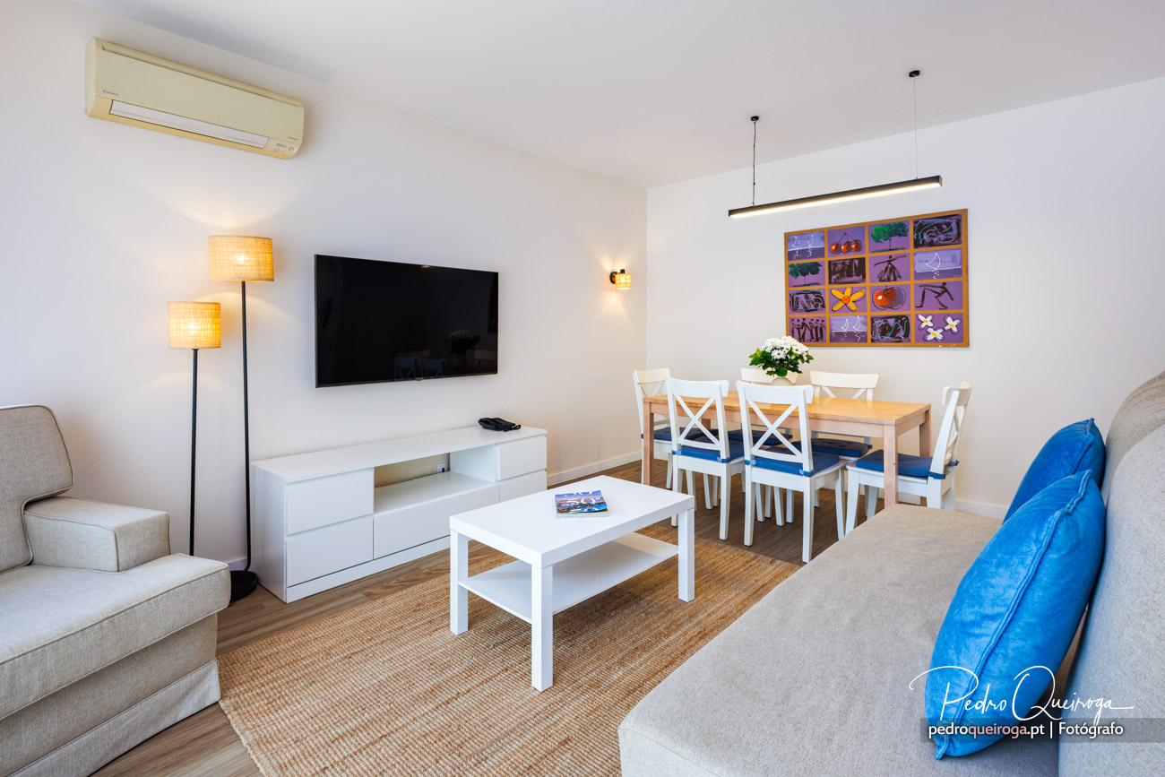 Sala de estar e jantar moderna com televisão, mesa de refeições, sofás bege e almofada azul vibrante