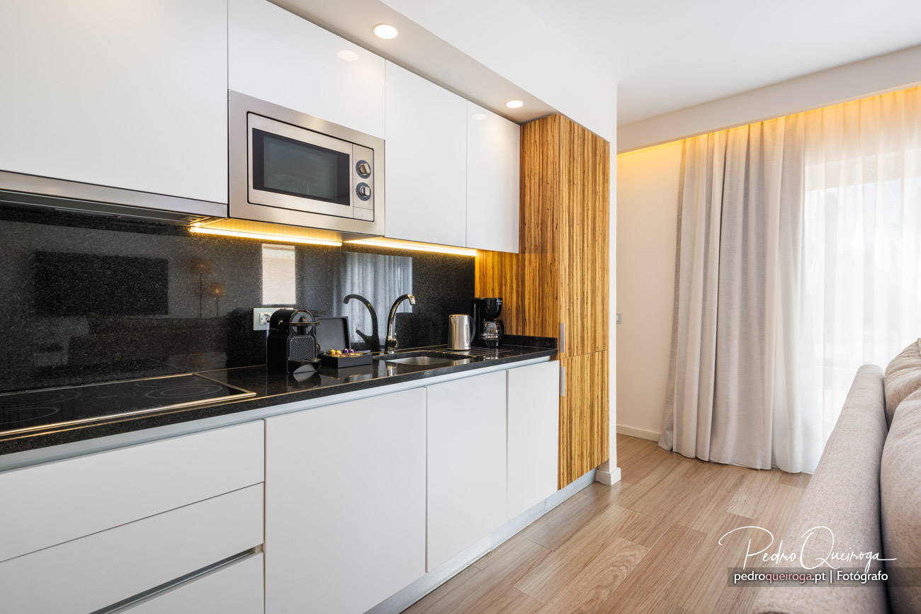 Cozinha moderna com armários brancos, bancada preta, painel em madeira e iluminação LED embutida