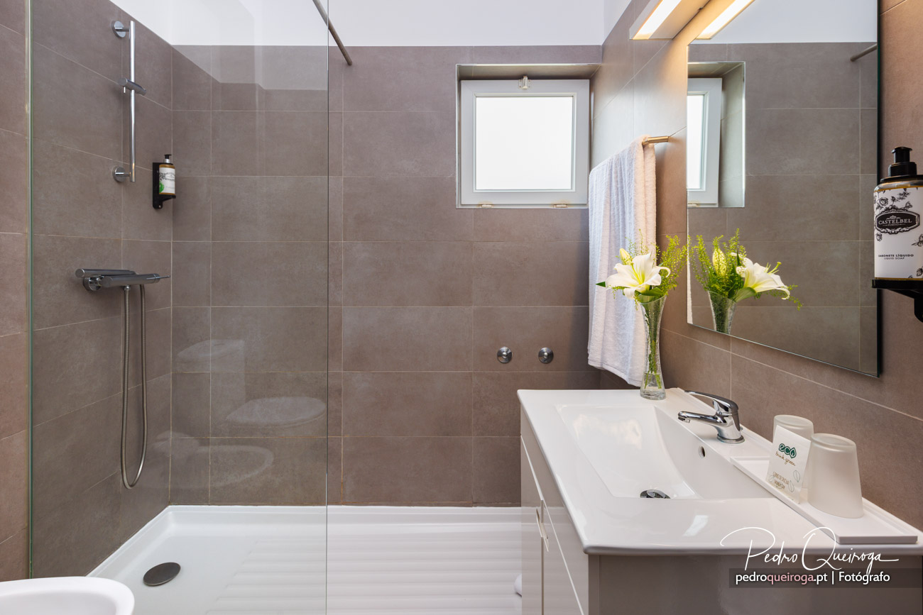 Casa de banho moderna com tons cinza, base de duche ampla e arquitetura clean com luz natural pela janela