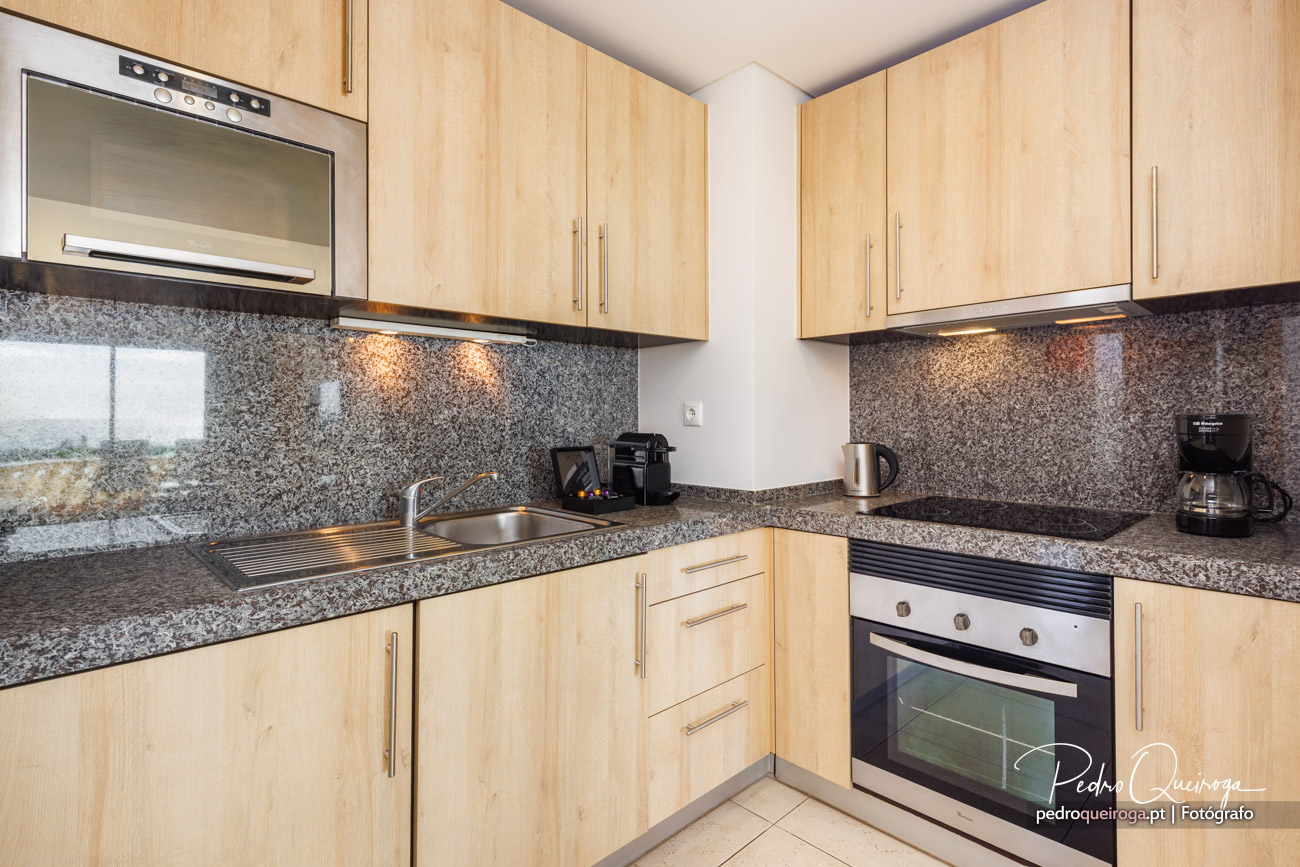Cozinha moderna com armários em madeira clara, bancada em granito e eletrodomésticos integrados num espaço luminoso.