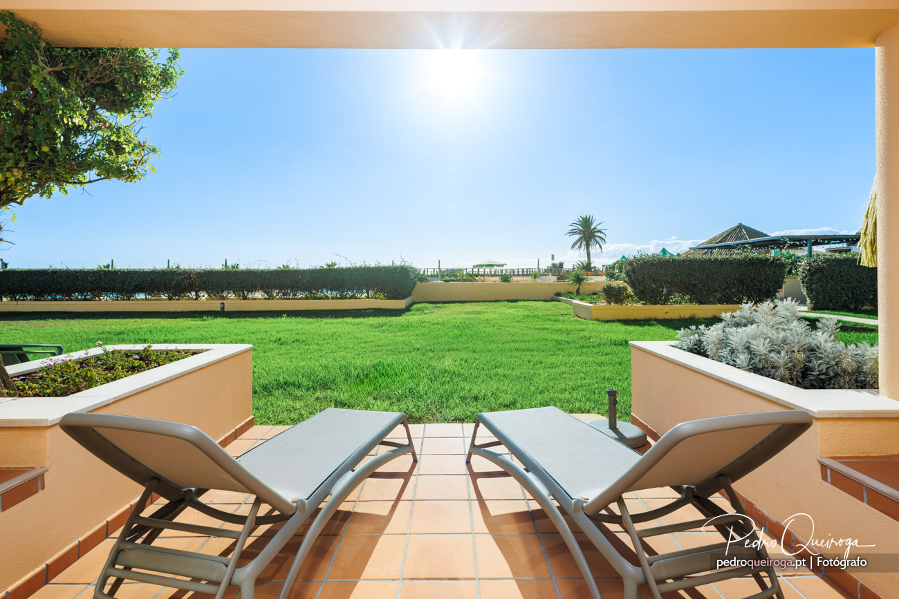Terraço privado com espreguiçadeiras viradas para jardim verdejante e céu azul em dia ensolarado