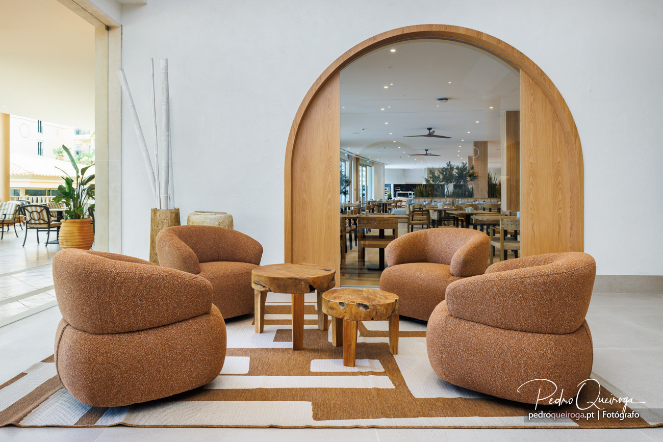 Sala de estar com sofás castanhos e arco em madeira que enquadra zona de refeições ao fundo