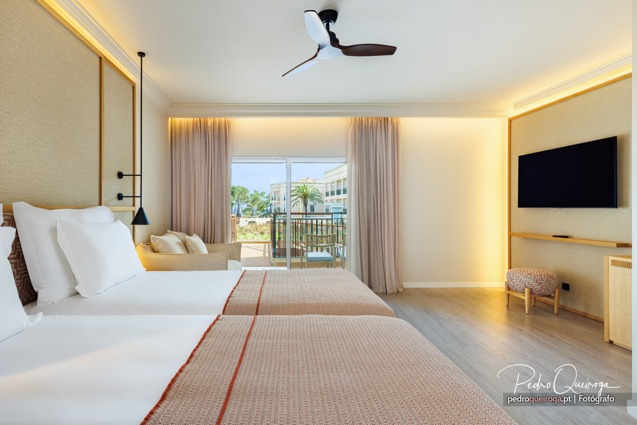 Quarto de hotel luminoso com cama king-size, varanda com vista para piscina e decoração em tons neutros e dourados