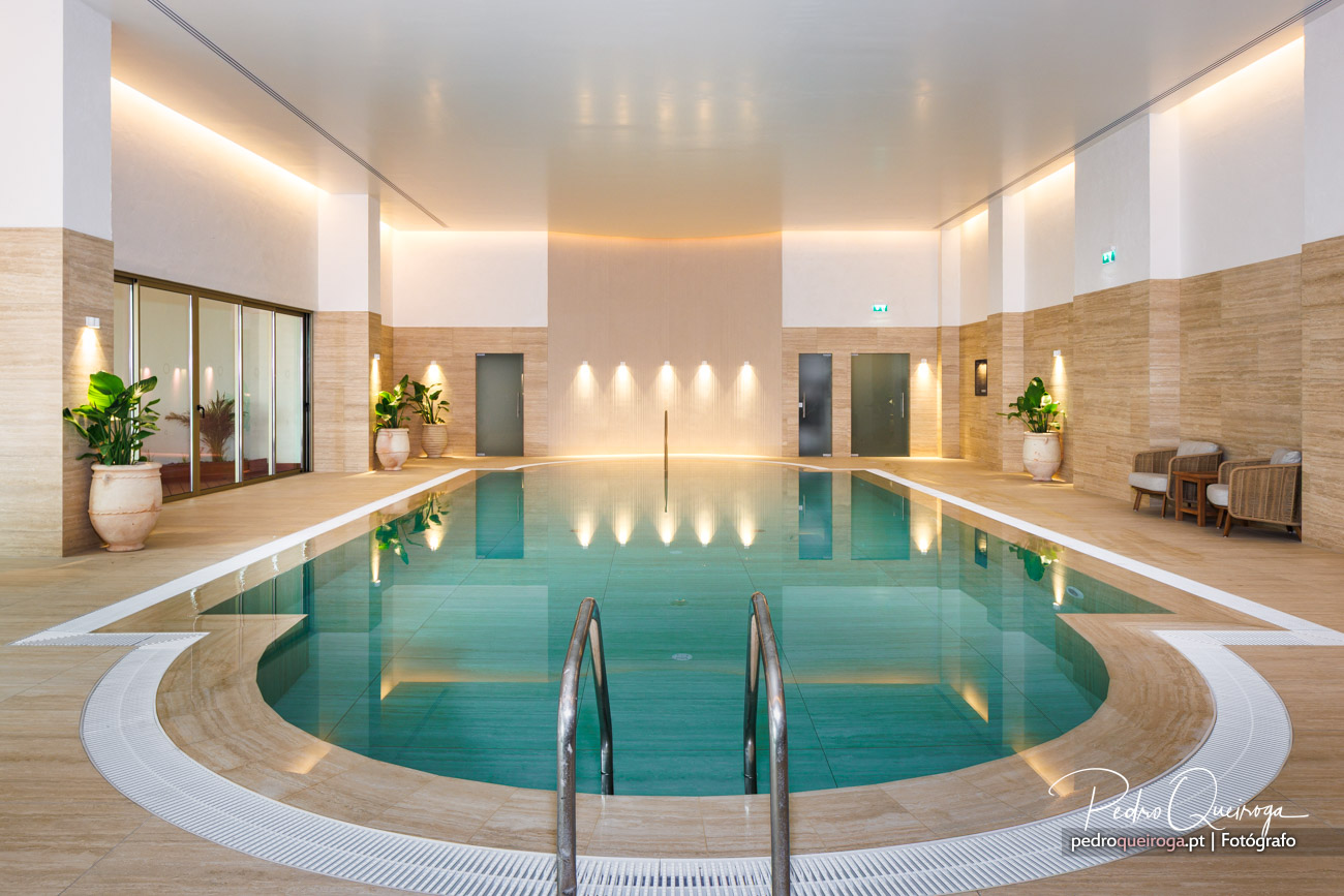 Piscina interior de design minimalista com água turquesa, revestimentos em madeira clara e iluminação ambiente suave