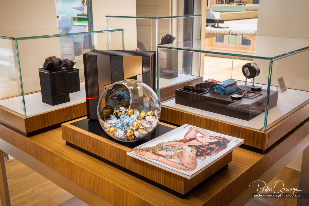 Expositor de loja com vitrinas de vidro, chocolates em esfera e amenities de hotel sobre madeira nobre