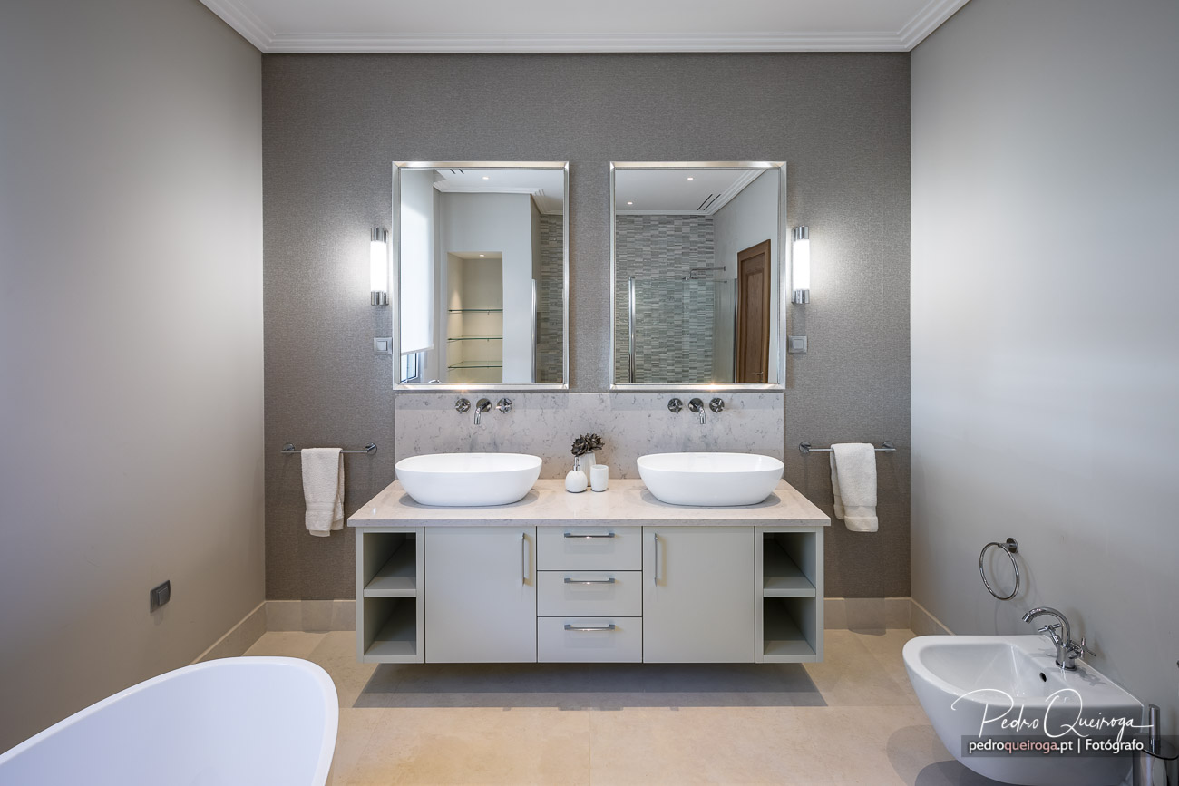 Casa de banho moderna com duplo lavatório oval, espelhos iluminados, móvel suspenso bege e parede texturizada cinzenta
